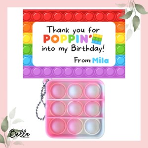May include: A colorful birthday-themed gift tag with the text "Thank you for POPPIN' into my Birthday! From: Mila." A pink and white pop-it toy with a silver chain is below the tag. The tag has a rainbow border.
