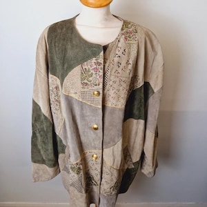 Op de afbeelding: Een vintage patchwork jas in tinten groen, beige en grijs, tentoongesteld op een mannequin. De jas heeft een ronde halslijn, gouden knopen en diverse stoffen patches met patronen. De algehele stijl is een uniek, retro ontwerp.
