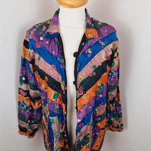 May include: A patchwork jacket in a vibrant mix of floral and striped patterns. The jacket has a collared neckline, long sleeves, and three black buttons. The colour palette includes purple, blue, orange, and green.