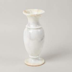 May include: A tall, slender vase crafted from polished white stone with subtle grey veining throughout. The vase features a flared rim, a narrow neck, a rounded body, and a circular pedestal base, showcasing a smooth, glossy finish and natural stone patterns.