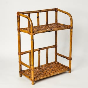 May include: A two-tier shelf unit constructed from brown bamboo poles with a woven bamboo lattice pattern on both the top and bottom surfaces. The structure features vertical supports and curved side rails, showcasing a natural wood finish.