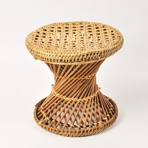 May include: A round stool constructed from light brown woven rattan. The seat features a flat, intricate cane weave pattern, while the base is formed by a hourglass-shaped structure of diagonal rattan reeds that taper toward the center.