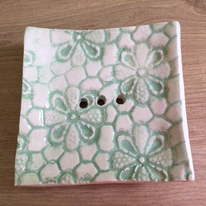 May include: A white ceramic soap dish with a green floral design. The dish has three drainage holes.