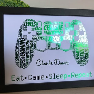 May include: A framed green and white word art print of a video game controller with the words "Eat Game Sleep Repeat" and the name "Charlie Davies" below the controller.