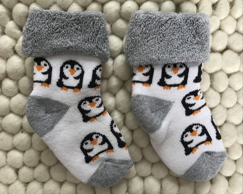 Op de afbeelding: Een paar witte babysokken met een grijze boord en pingu&iuml;nontwerpen. De sokken hebben een grijze hiel en teen.