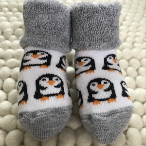 Op de afbeelding: Een paar witte babysokken met een pingu&iuml;npatroon. De sokken hebben een grijze, pluche boord.