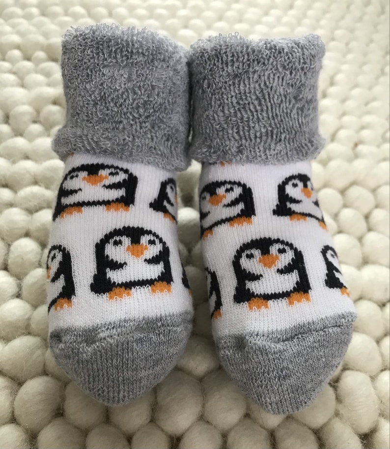 Op de afbeelding: Een paar witte babysokken met een pingu&iuml;npatroon. De sokken hebben een grijze, pluche boord.