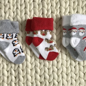 Op de afbeelding: Drie paar kerstsokken voor baby's. E&eacute;n paar heeft pingu&iuml;ns, een ander paar heeft rendieren en het laatste paar heeft kerstmannen.