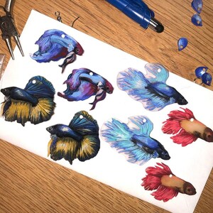 May include: Eight colorful hand-painted betta fish ornaments. The fish are painted in shades of blue, red, yellow, and purple. The ornaments are perfect for adding a touch of whimsy to any space.