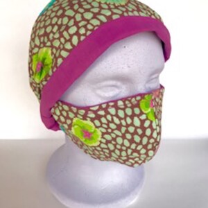 May include: A pink and brown patterned surgical scrub hat with a matching face mask. The hat has a pink trim and the mask has a brown and green floral pattern.