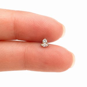 May include: A gold stud earring featuring a small round brilliant-cut clear gemstone positioned above a marquise-cut clear gemstone. The two stones are set in a gold metal base, creating a stacked, elongated design for a piercing.