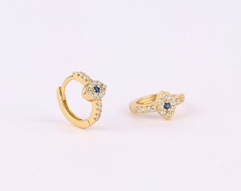 May include: A pair of gold hoop earrings with a blue evil eye charm. The earrings are set with small clear cubic zirconia stones.