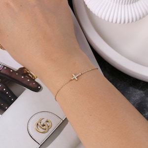 May include: A gold chain bracelet with a small, diamond-encrusted cross charm.