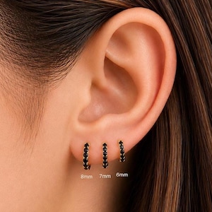 May include: Three gold hoop earrings with black stones are displayed on an ear. The earrings are labeled 8mm, 7mm, and 6mm. The ear is set against a blurred background.