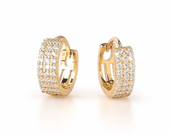 May include: A pair of gold-colored hoop earrings. Each earring is encrusted with multiple rows of small, clear gemstones. The earrings have a hinged closure and a polished finish, reflecting light. The design is simple yet elegant.