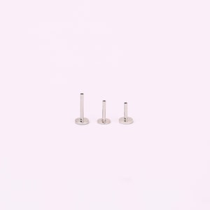 May include: Three silver-toned metal labret studs arranged in a row, each featuring a flat circular base and a hollow cylindrical post of varying heights, designed for body piercing jewelry with a smooth, polished, and reflective metallic finish.
