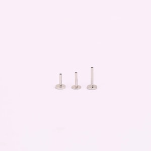 May include: Three silver-colored metal labret studs with flat circular bases and hollow cylindrical posts of varying lengths. Each piece features a smooth, polished finish and a simple, functional design intended for body piercing jewelry.