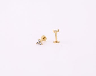 May include: A pair of gold-toned stud earrings with clear cubic zirconia stones. The earrings are in the shape of a triangle with three stones.