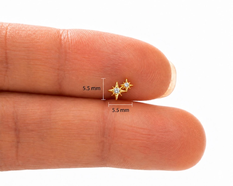 May include: A gold-toned stud earring featuring two connected star-shaped charms, each set with a small clear stone. The earring measures 5.5 mm in height and 5.5 mm in width as indicated by the measurement lines visible on the product.