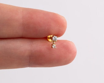 May include: A gold-tone stud earring featuring a small, round, clear gemstone set in a prong setting, with a second, smaller, round, clear gemstone dangling directly beneath it from a short, delicate gold-tone chain link.