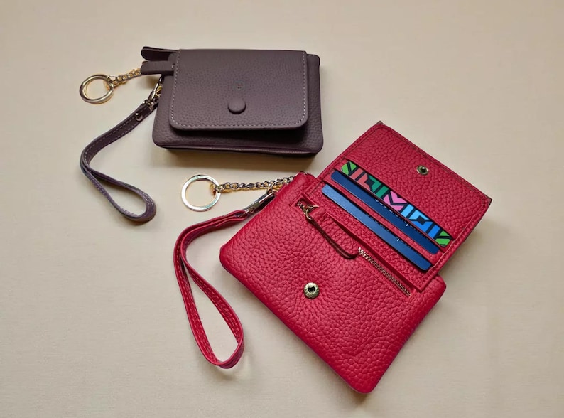 two leather wallet and keychain accessories, one in a dark brown color and the other in a vibrant red color, placed on a light-colored surface.