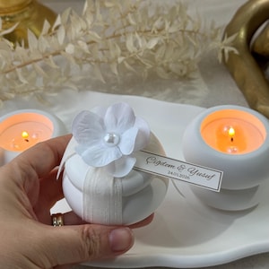 Peut inclure: Bougeoirs blancs avec des bougies allum&eacute;es. Un bougeoir est d&eacute;cor&eacute; d'une fleur blanche et d'un ruban. Une petite &eacute;tiquette indique "&Ccedil;iğdem & Yusuf 24.01.2026". Les bougies sont sur un plateau blanc.