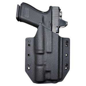 May include: Black polymer holster with a black handgun. The holster has multiple mounting holes and a textured surface. The handgun has a black slide and a red dot sight.