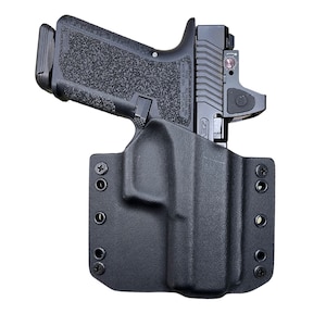May include: A black polymer holster with a black handgun inside. The holster has multiple attachment points and is designed for concealed carry.