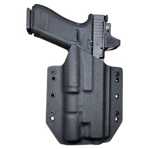 May include: A black handgun with a red dot sight is holstered in a black, textured polymer holster. The holster has multiple screw holes for attachment and a molded design to fit the firearm.