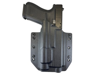 Puede incluir: Una funda de polímero negro para una pistola con un portacargador de polímero negro. La funda tiene varios tornillos en el lateral.