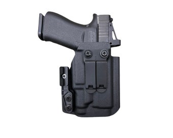 Puede incluir: Funda de polímero negro con una pistola. La funda tiene dos clips para cinturón y retención ajustable. La pistola es negra con un agarre texturizado. La imagen está sobre un fondo blanco.