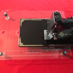 May include: A clear acrylic sewing table with a black sewing machine on top. The table has a ruler on the front edge and the text "www.tailormadetables.com" printed on the ruler.