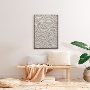 Pu&ograve; includere: Una stampa incorniciata nera di un design minimalista di arte di linee di onde in tonalit&agrave; di bianco e grigio appesa a una parete bianca sopra una panca di legno con una coperta beige e due cuscini bianchi. Una pianta in vaso con grandi foglie verdi si trova sul pavimento accanto alla panca.