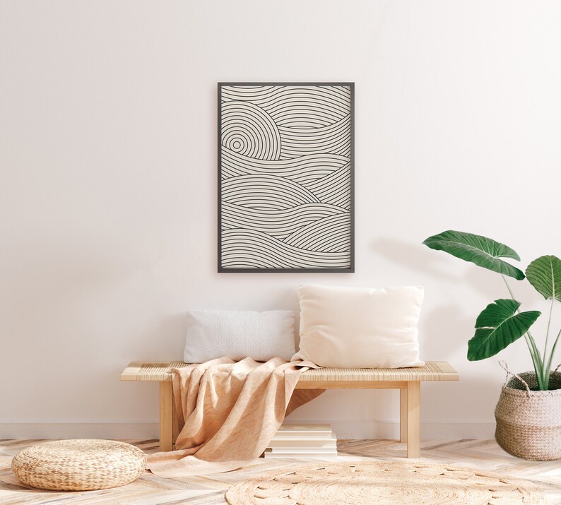 Pu&ograve; includere: Una stampa incorniciata nera di un design minimalista di arte di linee di onde in tonalit&agrave; di bianco e grigio appesa a una parete bianca sopra una panca di legno con una coperta beige e due cuscini bianchi. Una pianta in vaso con grandi foglie verdi si trova sul pavimento accanto alla panca.