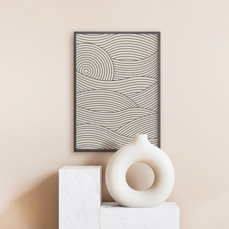 Pu&ograve; includere: Una stampa incorniciata nera di un design geometrico di arte lineare con onde astratte in color crema. Un vaso in ceramica bianca con un taglio circolare si trova su un piedistallo bianco.