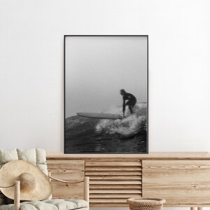 K&ouml;nnte beinhalten: Schwarzwei&szlig;foto von einem Surfer, der auf einer Welle reitet. Der Surfer tr&auml;gt einen Neoprenanzug und ist vor dem Himmel silhouettiert. Die Welle bricht und es gibt viel Gischt.