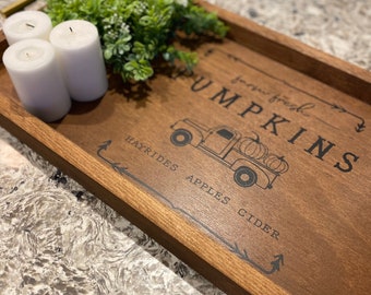 May include: A wooden tray with the text "Farm Fresh Pumpkins Hayrides Apples Cider" and a black and white illustration of a truck with pumpkins. Three white candles are on the tray with a small green plant.