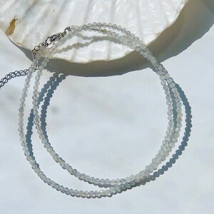 Peut inclure: Un collier délicat en chaîne argentée avec deux rangs de petites perles claires et facettées.