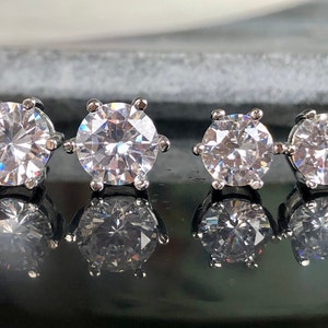 May include: Four pairs of silver stud earrings with clear round cubic zirconia stones. The stones are different sizes, with the largest stone on the left and the smallest stone on the right.