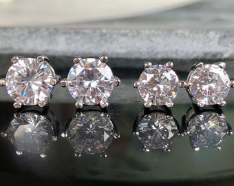 May include: Four pairs of silver stud earrings with clear round cubic zirconia stones. The stones are different sizes, with the largest stone on the left and the smallest stone on the right.