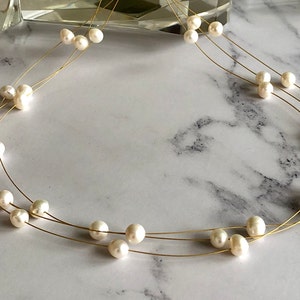 May include: A delicate gold necklace with three strands of pearls. The pearls are white and round, and they are evenly spaced along the strands.