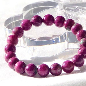 May include: A bracelet made of deep pink, round beads. The beads have a slightly mottled appearance, giving them a unique texture.