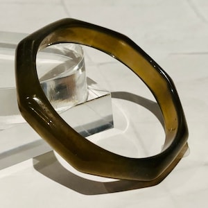 May include: A dark green octagonal bangle bracelet made of smooth, polished plastic.