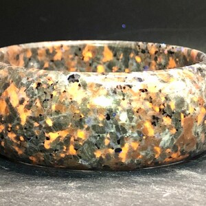 May include: A round, polished, green, black, and orange stone bangle bracelet. The stone has a speckled pattern.