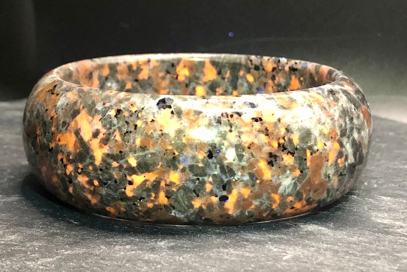 May include: A round, polished, green, black, and orange stone bangle bracelet. The stone has a speckled pattern.