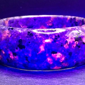 May include: A purple and pink gemstone bracelet with a speckled pattern. The bracelet is made of a smooth, polished stone.