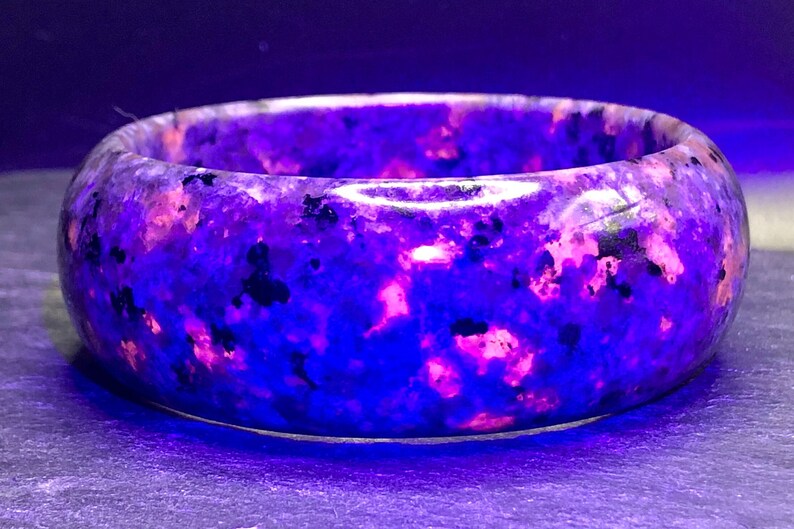 May include: A purple and pink gemstone bracelet with a speckled pattern. The bracelet is made of a smooth, polished stone.