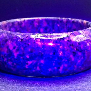 May include: A purple and pink speckled bangle bracelet made of stone. The bracelet is smooth and polished.