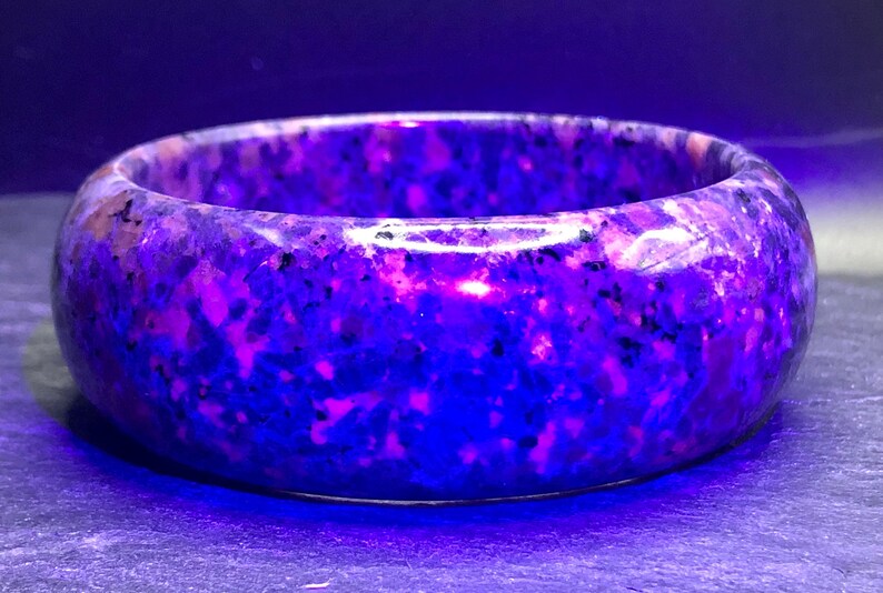 May include: A purple and pink speckled bangle bracelet made of stone. The bracelet is smooth and polished.