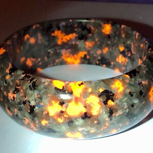 May include: A dark green and black bracelet with orange flecks. The bracelet is made of a natural stone and has a smooth, polished finish.